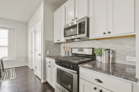 a kitchen with stainless steel appliances granite countertop white cabinets a stove top oven a sink and dishwasher