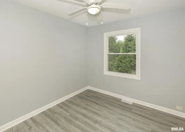 an empty room with wooden floor and fan