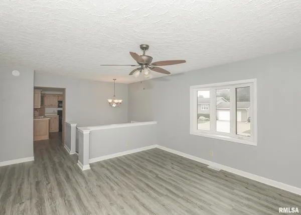 an empty room with wooden floor chandelier fan and windows