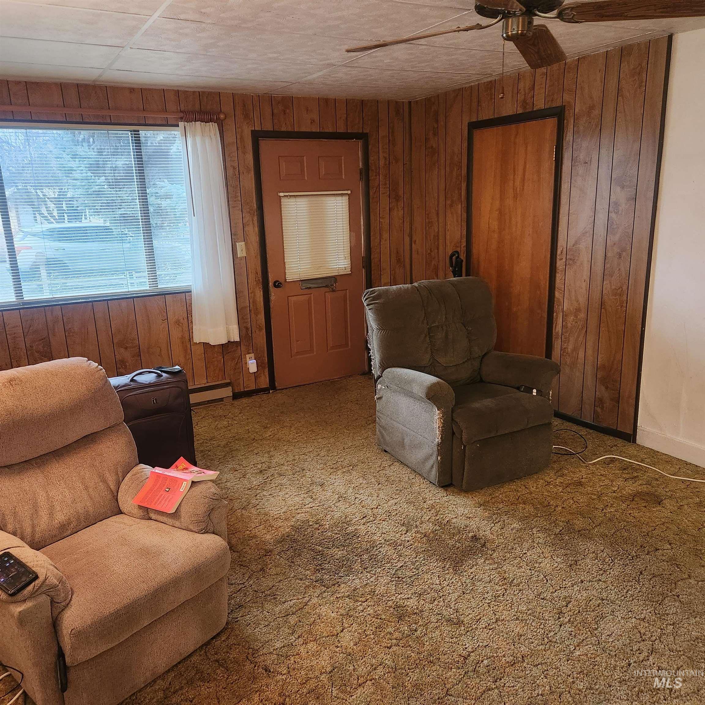 530 California Street Gooding, ID 83330 - Photo 3 of 30 Living area with wooden walls, ceiling fan, carpet, and a baseboard heating unit