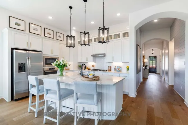 a kitchen with stainless steel appliances kitchen island granite countertop a refrigerator a stove a kitchen island and chairs with wooden floor