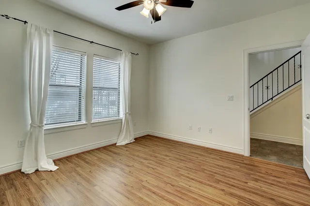an empty room with wooden floor chandelier fan and windows