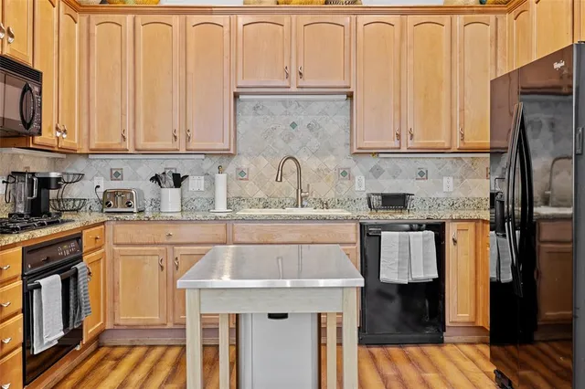 a kitchen with stainless steel appliances granite countertop a stove top oven a sink dishwasher a dining table and chairs with wooden floor