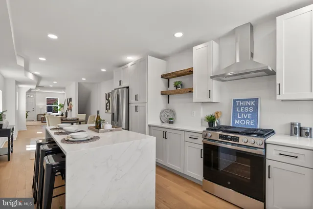 a kitchen with stainless steel appliances kitchen island granite countertop a stove a sink a refrigerator and white cabinets with wooden floor