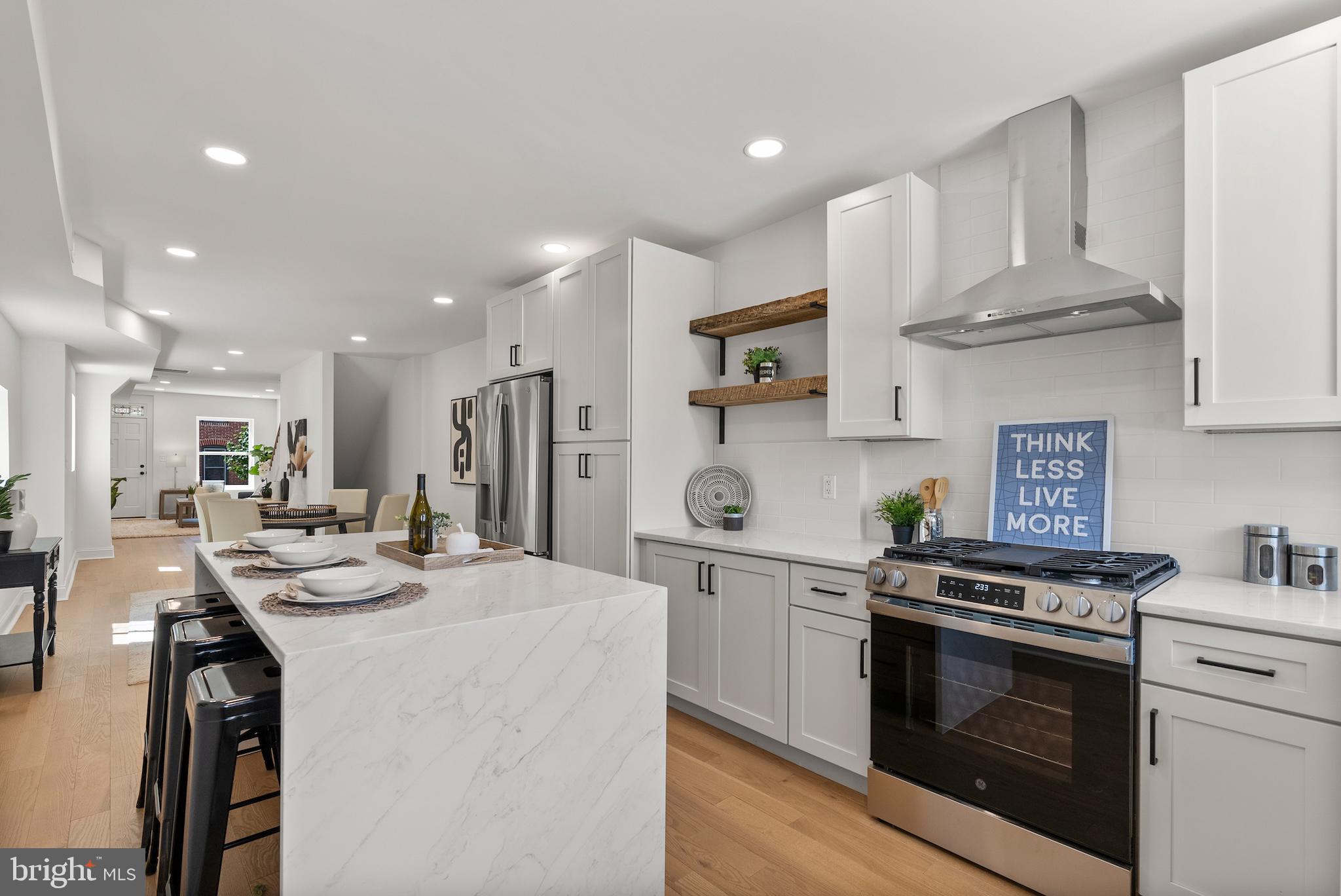 a kitchen with stainless steel appliances kitchen island granite countertop a stove a sink a refrigerator and white cabinets with wooden floor