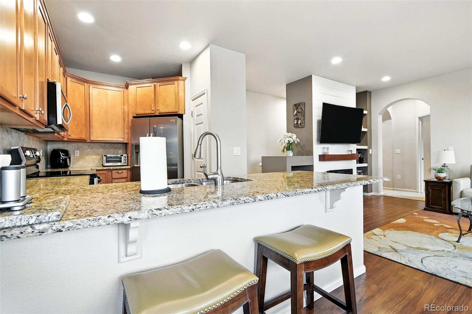 12804 Harrison Street Thornton, CO 80241 - Photo 12 of 37 a kitchen with stainless steel appliances granite countertop a stove top oven a sink a dining table and chairs with wooden floor