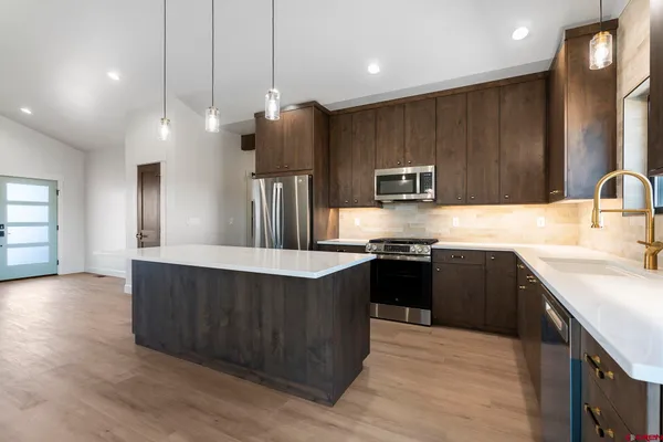a kitchen with stainless steel appliances wooden cabinets a sink dishwasher a stove and a refrigerator with wooden floor