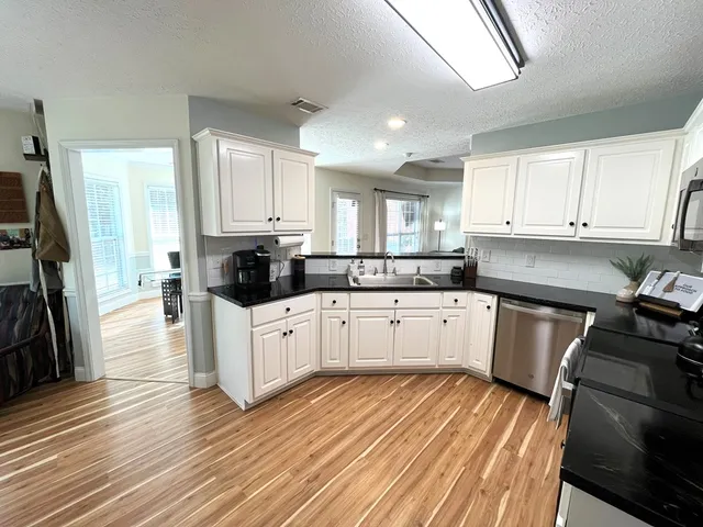 a kitchen with stainless steel appliances a stove top oven a sink a refrigerator white cabinets and wooden floor