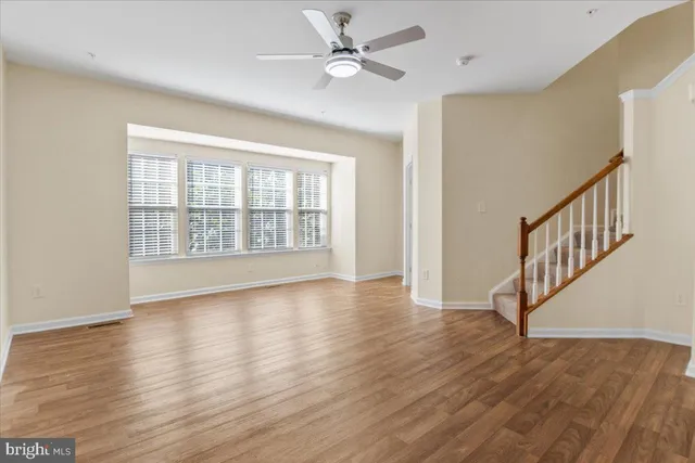 a view of an empty room with wooden floor and a ceiling fan