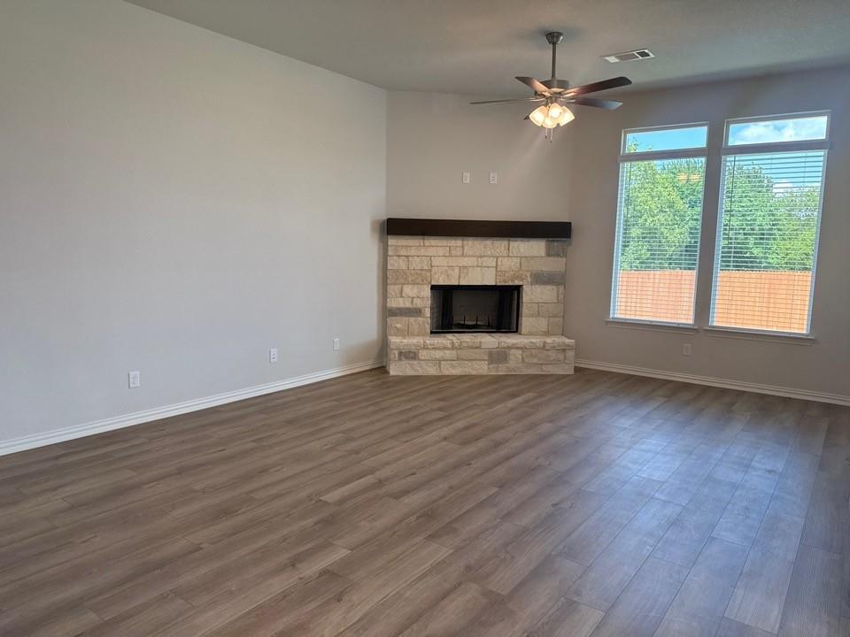 1233 Frio Drive Springtown, TX 76082 - Photo 6 of 13 Spacious living area featuring wood-finish flooring, a stone fireplace with a substantial wood mantel, multiple large windows with blinds, and a ceiling fan