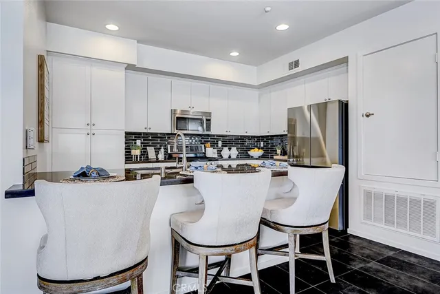 a kitchen with stainless steel appliances granite countertop a dining table chairs refrigerator and microwave