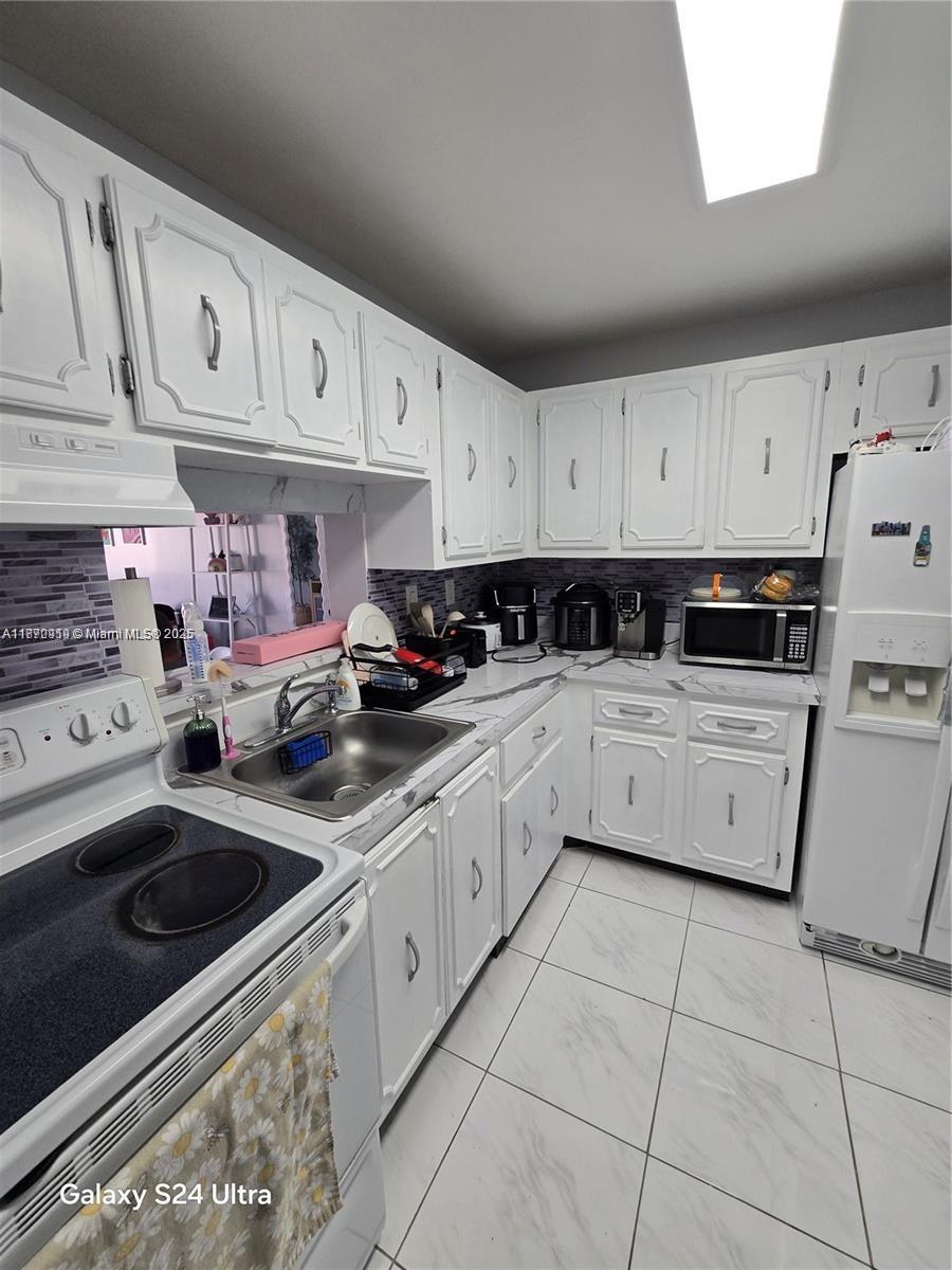 5201 Northwest 7th Street, Unit 609W Miami, FL 33126 - Photo 5 of 11 a kitchen with white cabinets a sink dishwasher and a stove with wooden floor