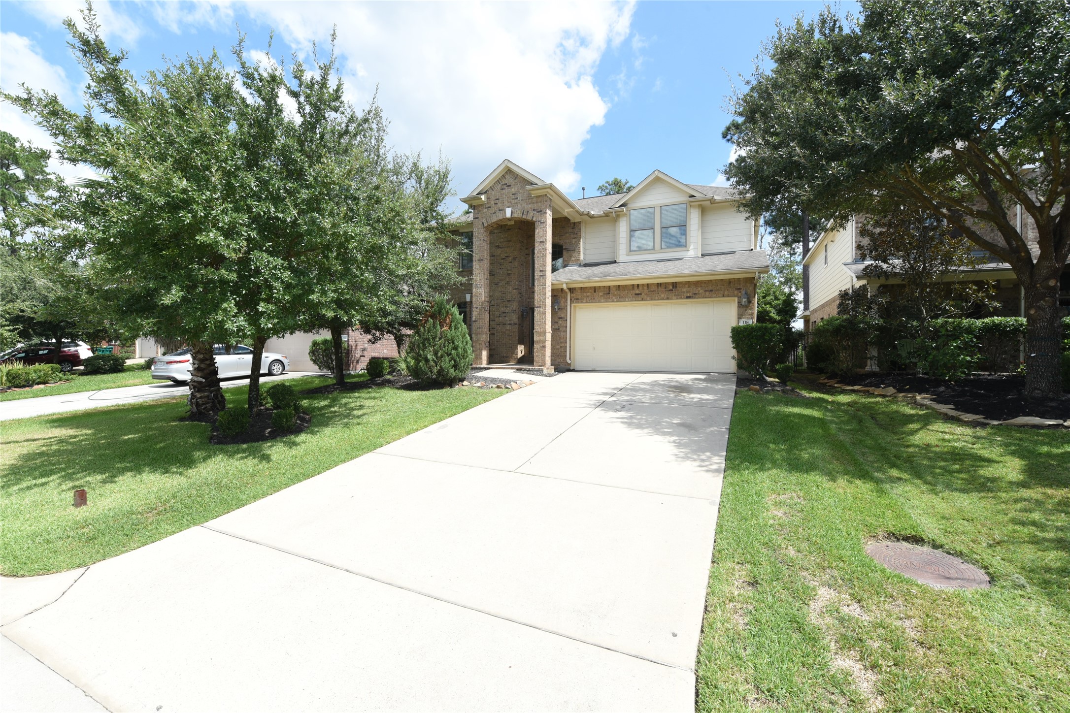 Charming two-story home with a spacious driveway, lush green lawn, and mature trees offering excellent curb appeal.