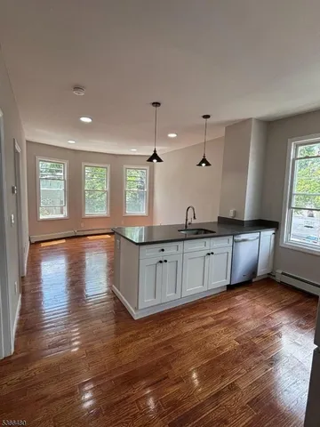 a kitchen with granite countertop a stove a sink and white cabinets with wooden floor next to windows
