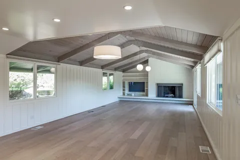 an empty room with wooden floor fireplace and windows