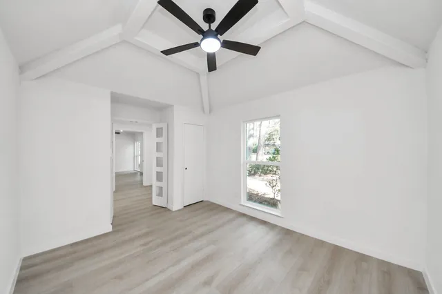 an empty room with wooden floor chandelier fan and windows