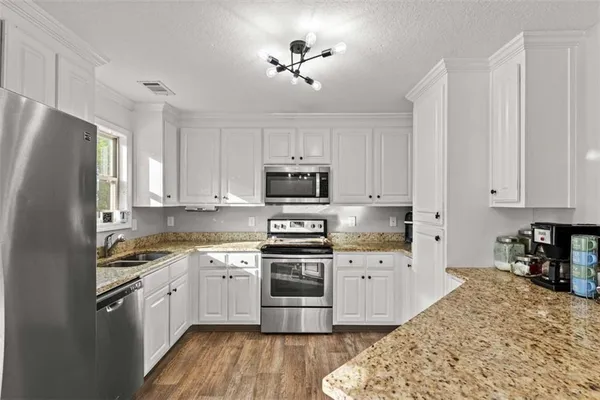 a kitchen with stainless steel appliances white cabinets a sink a stove a refrigerator and microwave with wooden floor