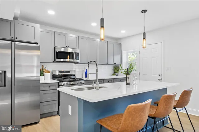 a kitchen with stainless steel appliances a sink a stove a refrigerator a center island and chairs