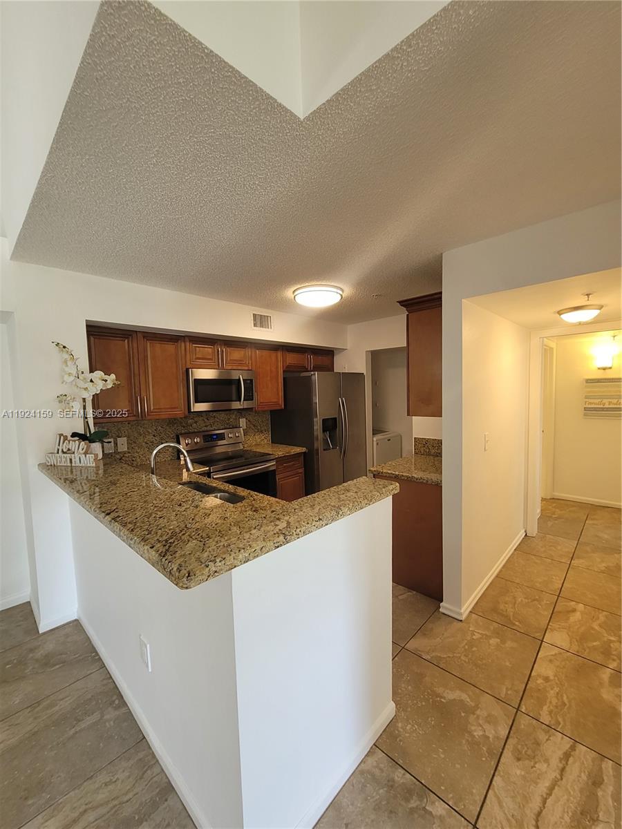 2133 Renaissance Boulevard, Unit 306 Miramar, FL 33025 - Photo 3 of 32 a large kitchen with kitchen island a sink a counter top and stainless steel appliances