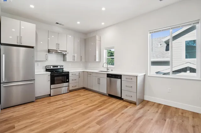 a kitchen with granite countertop a refrigerator oven a sink dishwasher and white cabinets with wooden floor