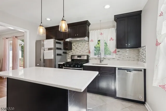 a kitchen with stainless steel appliances a sink a stove a refrigerator a center island and wooden cabinets