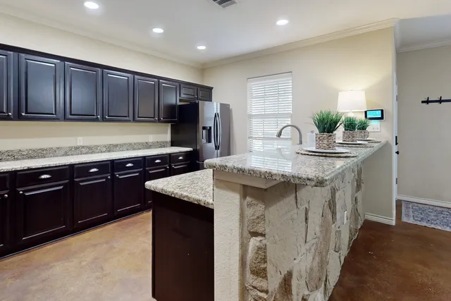 a kitchen with kitchen island granite countertop wooden cabinets a refrigerator and a sink