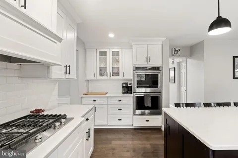 a kitchen with stainless steel appliances granite countertop a refrigerator a sink dishwasher a stove and a dining table with wooden floor
