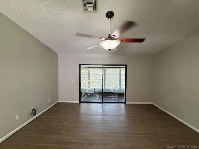 an empty room with wooden floor chandelier fan and windows