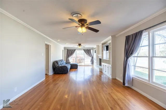 a view of a livingroom with wooden floor a ceiling fan and windows