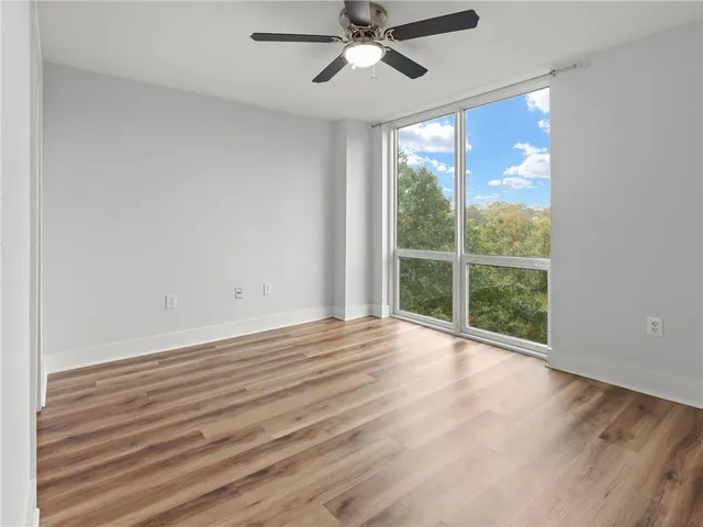 a view of an empty room with wooden floor and a ceiling fan