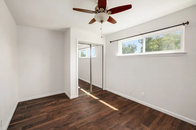 an empty room with wooden floor chandelier fan and windows