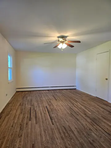 a view of an empty room with wooden floor and a chandelier fan