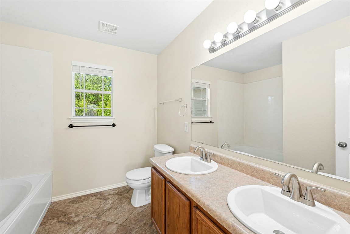 17913 Honey Locust Lane Elgin, TX 78621 - Photo 20 of 31 a bathroom with a granite countertop sink a toilet a mirror and a tub