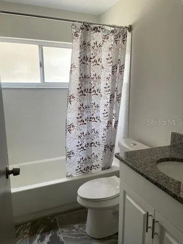 a bathroom with a granite countertop bathtub sink vanity mirror and toilet