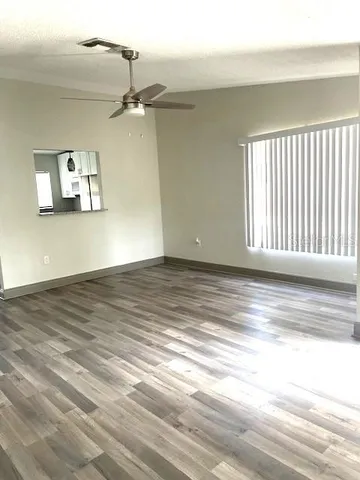 an empty room with wooden floor ceiling fan and windows