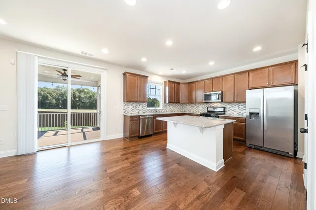 a kitchen with stainless steel appliances granite countertop a refrigerator a sink dishwasher a stove top oven a large island with wooden floor and cabinets