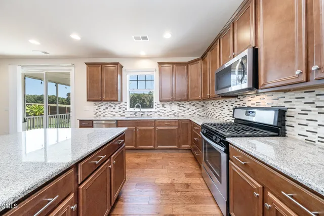 a kitchen with stainless steel appliances granite countertop wooden cabinets a stove top oven a sink and dishwasher with wooden floor