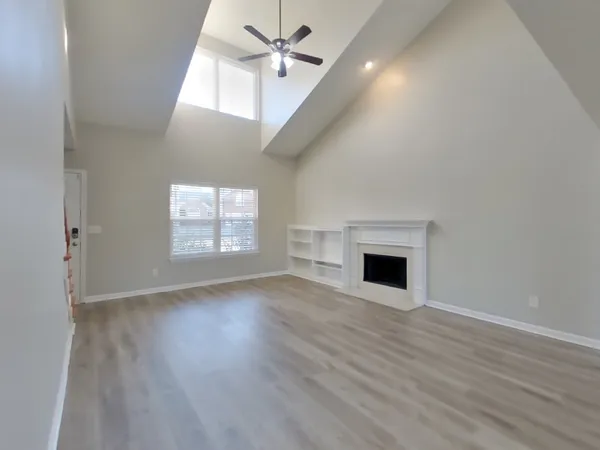 an empty room with wooden floor fan and windows