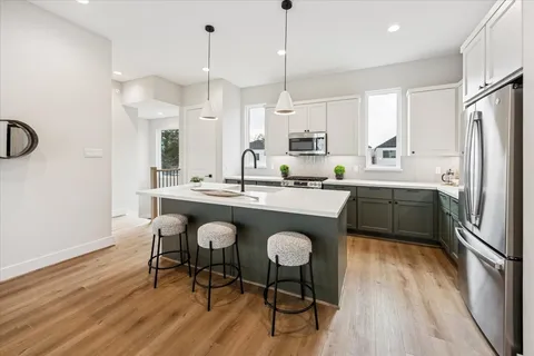 a kitchen with stainless steel appliances granite countertop a sink a stove a refrigerator and island with wooden floor