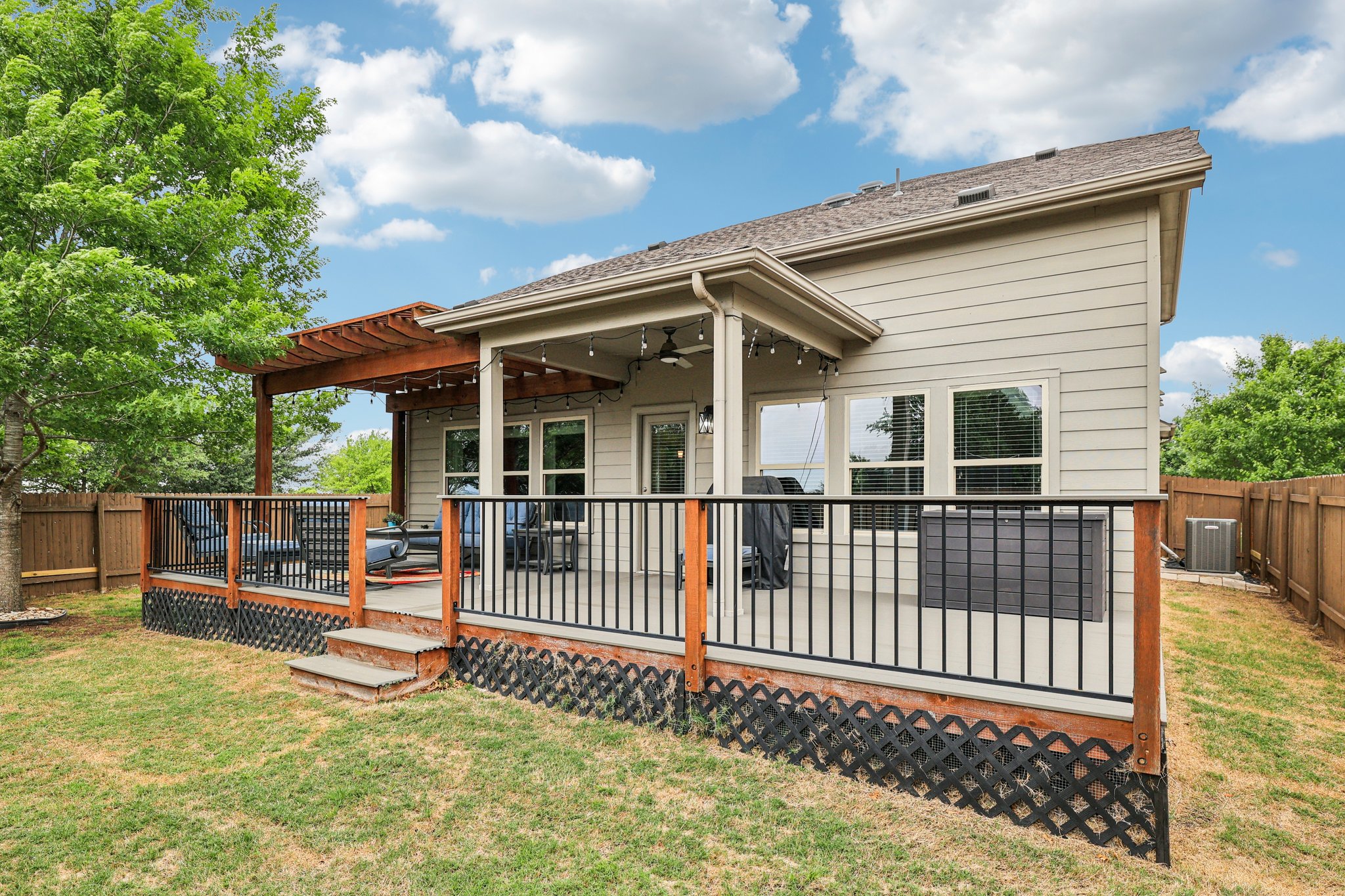 10033 Gertrudis Loop Austin, TX 78747 - Photo 27 of 39 The property features a spacious rear deck with wooden railings and black balusters, partially covered by an extension of the roof and a separate wooden pergola