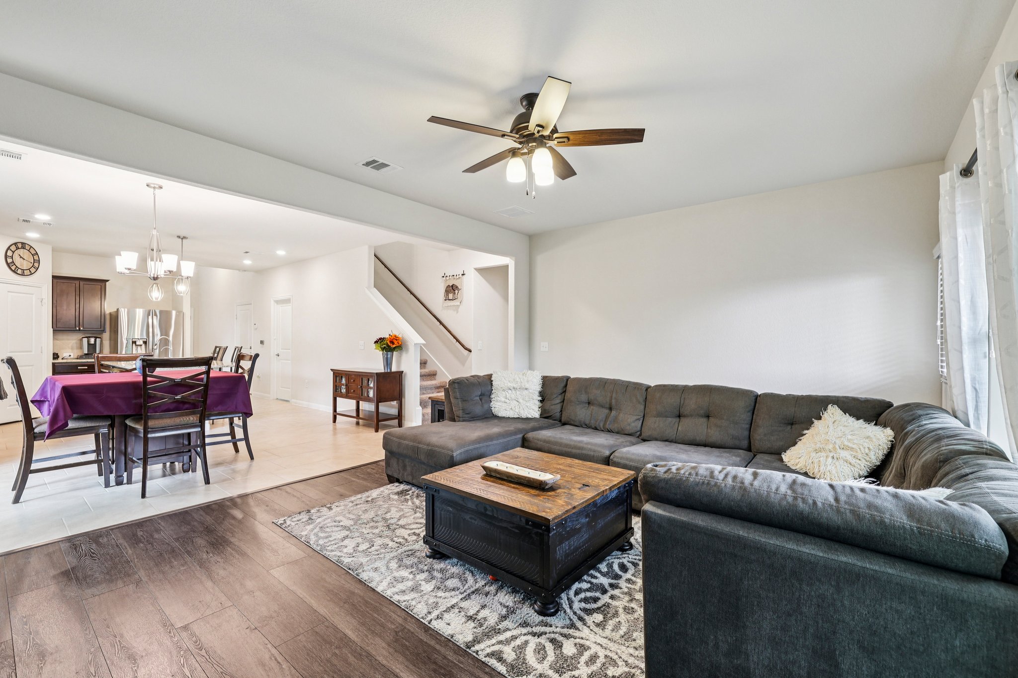 10033 Gertrudis Loop Austin, TX 78747 - Photo 31 of 39 Living room with dark wood flooring and a ceiling fan, opening to a dining area with light-colored flooring, and a stairway with a dark handrail