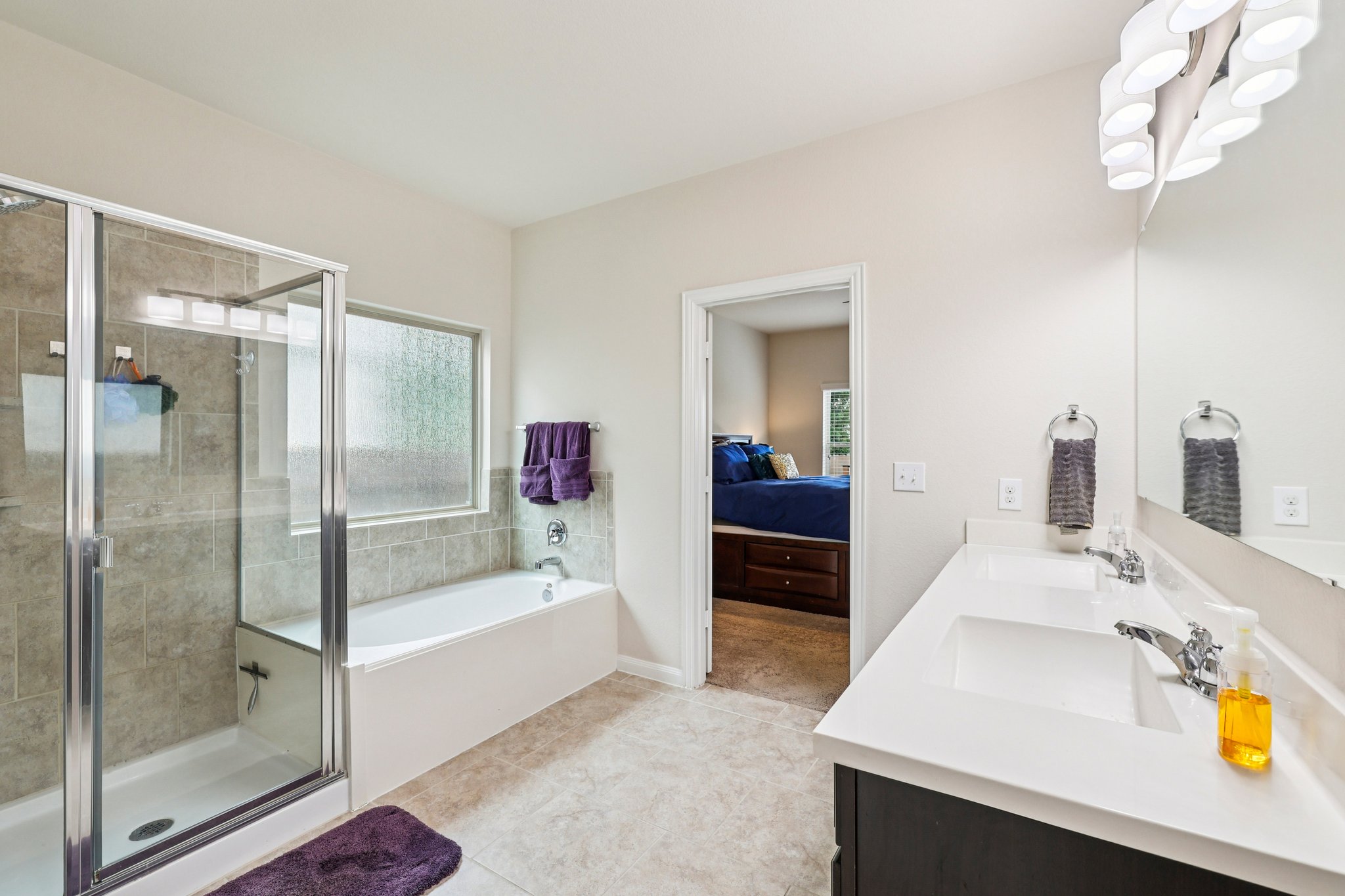 10033 Gertrudis Loop Austin, TX 78747 - Photo 33 of 39 The bathroom features a dual vanity with white countertops, a large mirror, a separate shower with a glass enclosure, and a bathtub with tiled surround