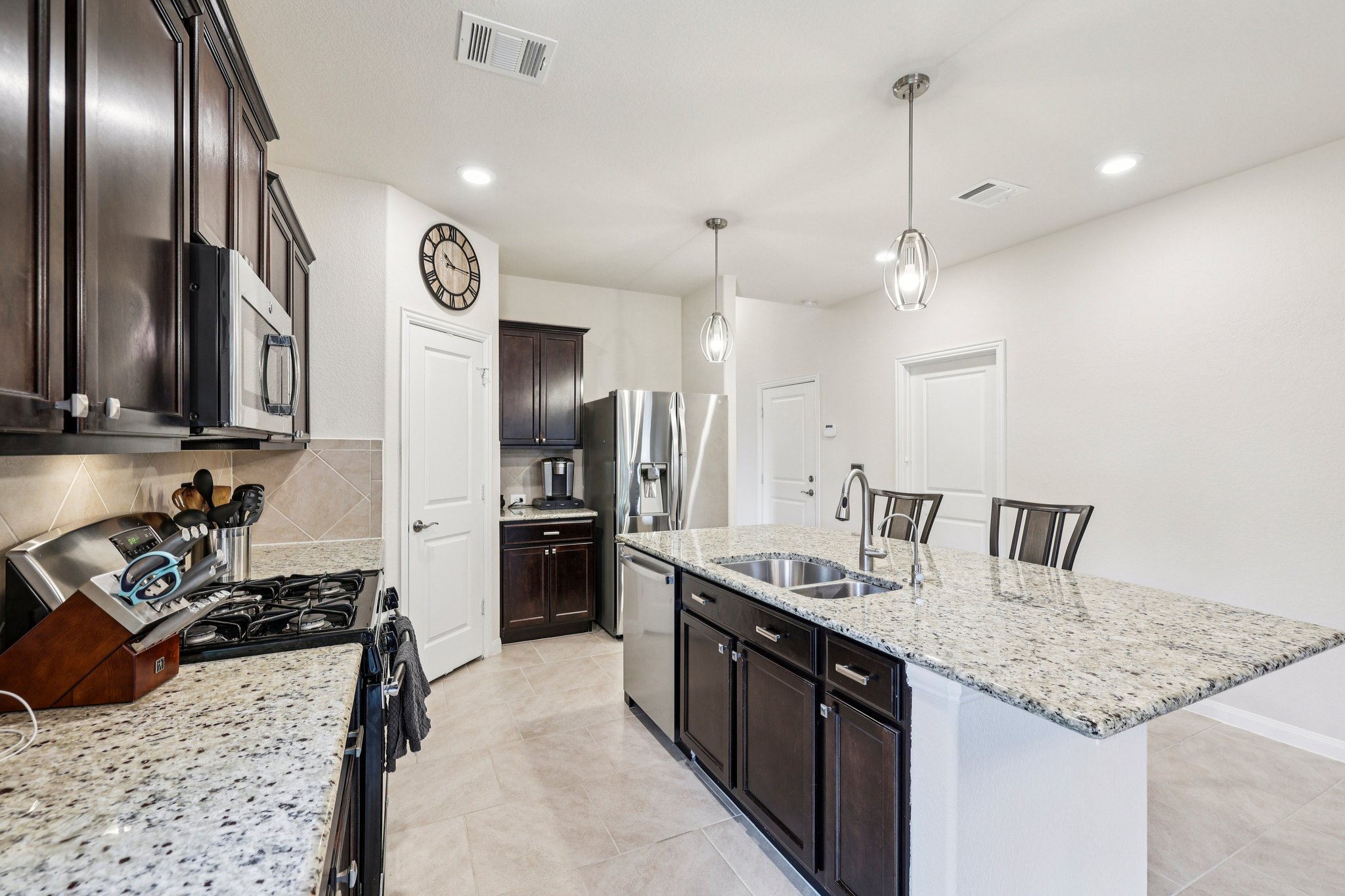 10033 Gertrudis Loop Austin, TX 78747 - Photo 6 of 39 This kitchen features a large island with a double sink and granite countertops, dark wood cabinetry, and stainless steel appliances