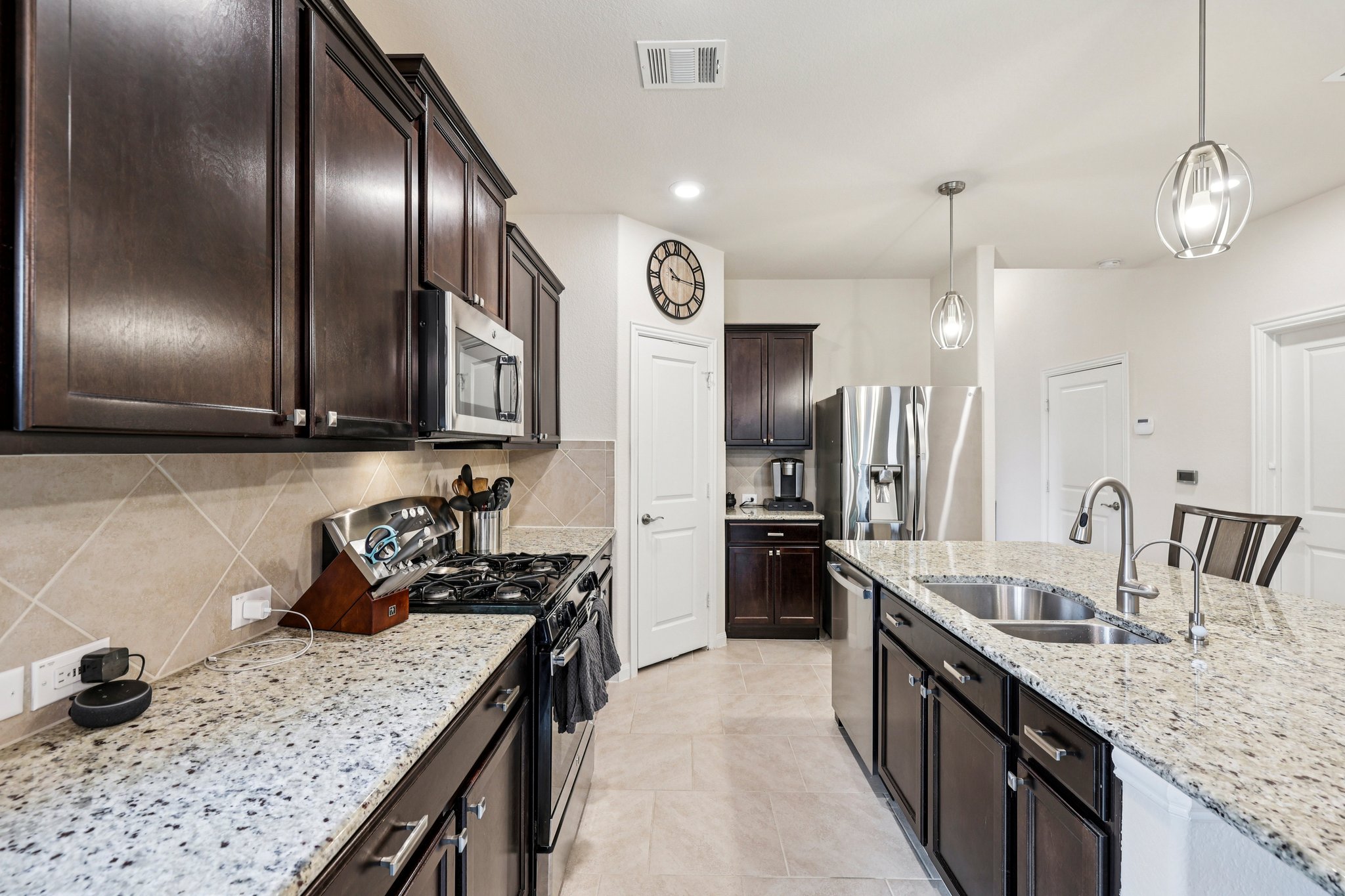 10033 Gertrudis Loop Austin, TX 78747 - Photo 7 of 39 The kitchen features dark wood cabinetry, stainless steel appliances, speckled countertops, and a tiled backsplash