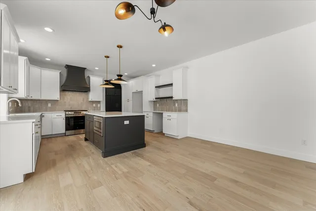 a open kitchen with kitchen island a stove a sink a refrigerator and white cabinets with wooden floor