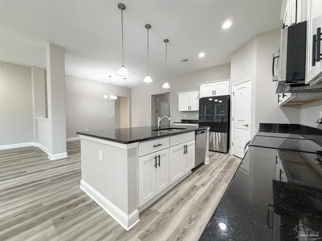 a kitchen with stainless steel appliances kitchen island granite countertop a refrigerator a oven a sink and white cabinets with wooden floor