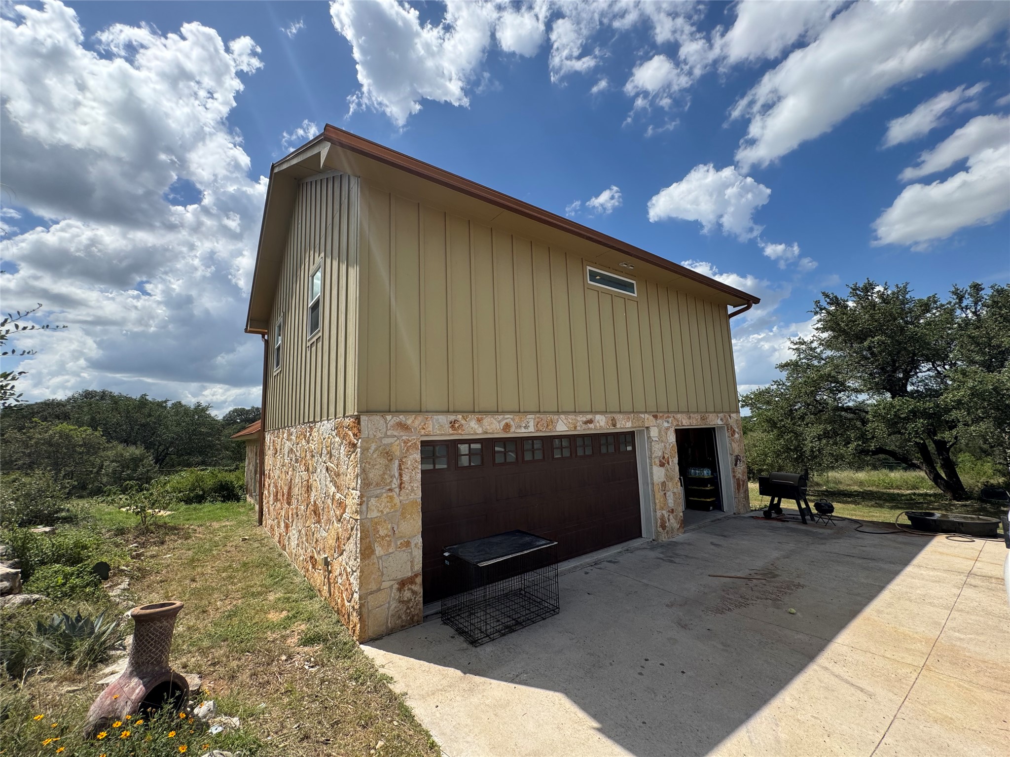3633 Outback Trail Spicewood, TX 78669 - Photo 5 of 34 View of property exterior featuring stone siding, an attached garage, driveway, and board and batten siding