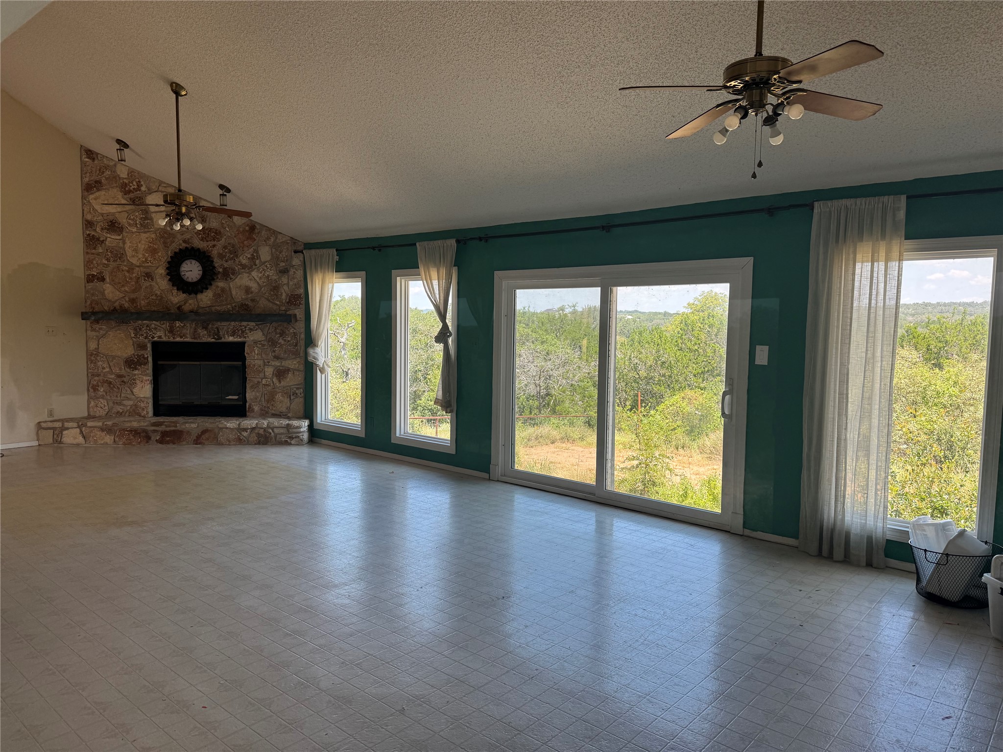 3633 Outback Trail Spicewood, TX 78669 - Photo 6 of 34 Unfurnished living room featuring a ceiling fan, a textured ceiling, a stone fireplace, and vaulted ceiling