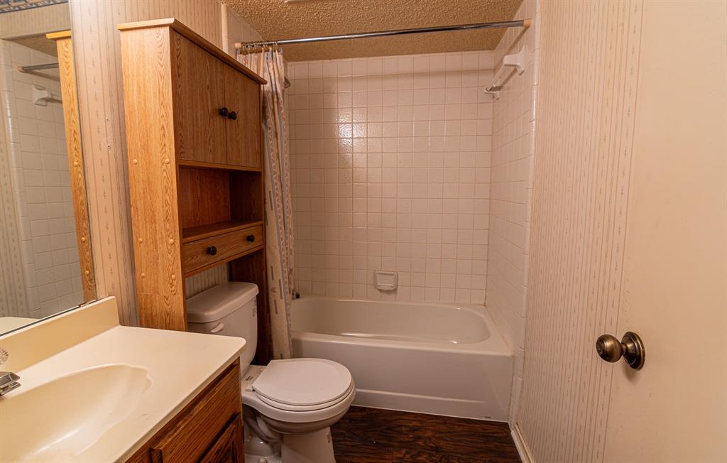 2028 Falcon Ridge Drive, Unit B Carrollton, TX 75010 - Photo 8 of 11 Full bath with vanity, a textured ceiling, shower / bath combo with shower curtain, and dark wood-style flooring