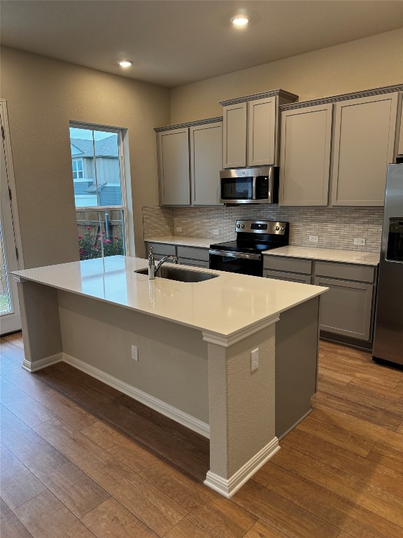 1020 Vista View Drive, Unit 2502 Georgetown, TX 78626 - Photo 2 of 15 Kitchen with gray cabinetry, appliances with stainless steel finishes, dark wood-style floors, decorative backsplash, and an island with sink